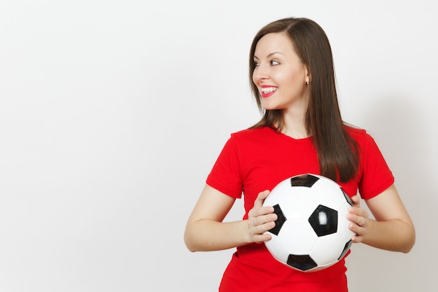 Mooie Europese jonge vrolijke gelukkige vrouw, voetbalfan of speler in rood uniform met klassieke voetbal geïsoleerd op een witte achtergrond. Sport, voetbal, gezondheid, gezond levensstijlconcept.