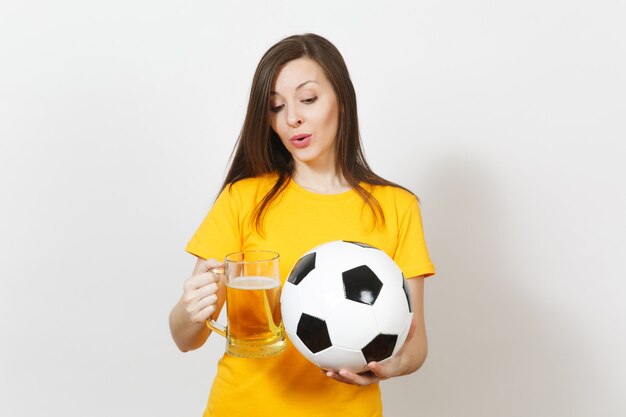 Mooie Europese jonge vrolijke vrouw, voetbalfan of speler in geel uniform met pint mok bier, voetbal geïsoleerd op een witte achtergrond. Sport, voetbal, gezond levensstijlconcept.