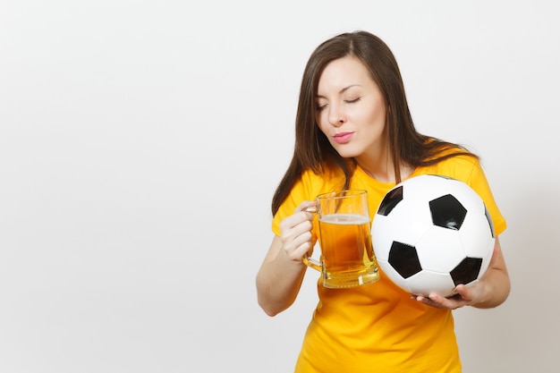 Mooie Europese jonge vrolijke vrouw, voetbalfan of speler in geel uniform met pint mok bier, voetbal geïsoleerd op een witte achtergrond. Sport, voetbal, gezond levensstijlconcept.