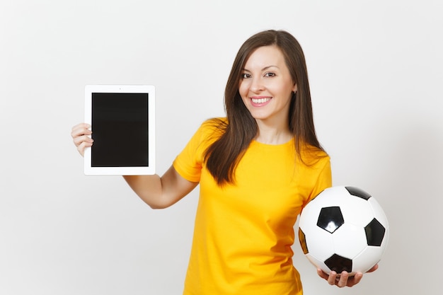 Mooie Europese jonge vrolijke vrouw, voetbalfan of speler in gele uniform houden tablet pc, voetbal geïsoleerd op een witte achtergrond. Sport, voetbal, gezondheid, gezond levensstijlconcept.