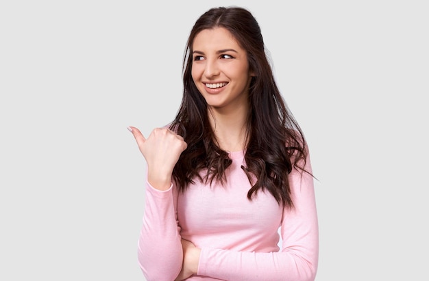 Mooie Europese jonge vrouw die een casual roze shirt met lange mouwen draagt, wat aangeeft dat ze lege kopieerruimte heeft voor reclametekst opzij kijkend en glimlachend poserend over een witte studioachtergrond