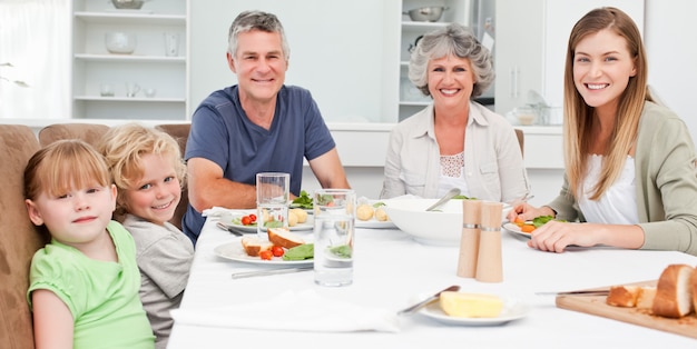 Mooie familie die de camera bekijkt terwijl het eten van hun maaltijd