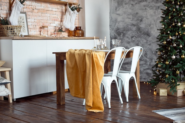 Mooie feestelijk ingerichte kamer in Scandinavische stijl, een feestelijke tafel met een tafel en een kerstboom met geschenken eronder.