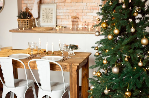 Mooie feestelijk ingerichte kamer in Scandinavische stijl, een feestelijke tafel met een tafel en een kerstboom met geschenken eronder