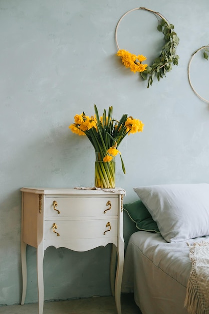 Mooie felgele tulpen in een glazen vaas staan op een barok nachtkastje bij een bed in pastelkleuren