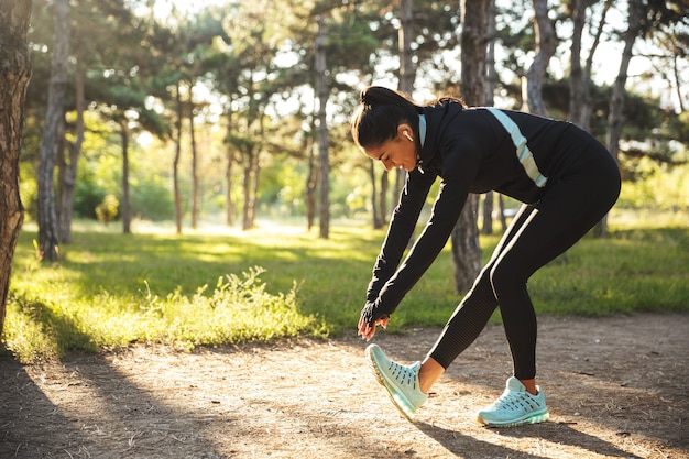 Foto mooie fit sportvrouw warming-up oefeningen doen voordat joggen in het park, luisteren naar muziek met koptelefoon
