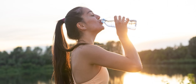 Mooie fitness atleet vrouw drinkwater na training oefenen op zonsondergang avond zomer in strand buiten portret.