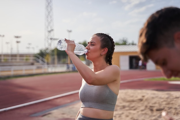 Mooie fitness atleet vrouw rustend drinkwater na het trainen op atletiekbaan in zonnige zonneschijn buiten