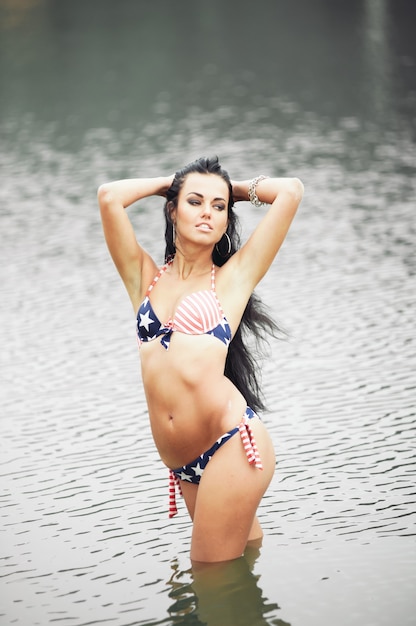 Mooie fitness jonge vrouw in zwembroek met amerikaanse vlag op het strand