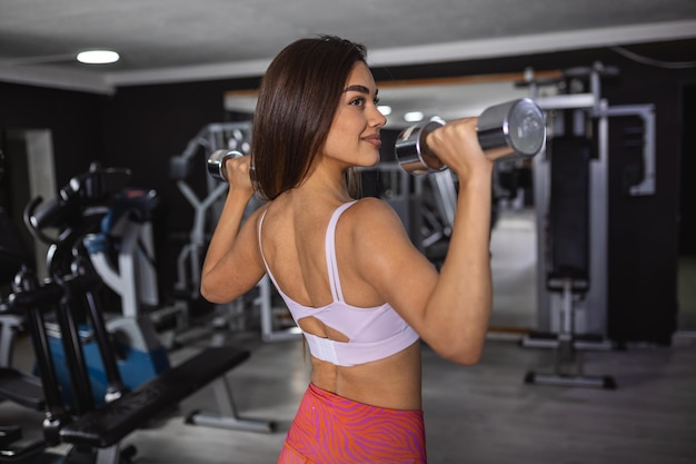 Mooie fitness vrouw met dumbbells opheffen Sportief meisje toont haar goed getraind lichaam Goed ontwikkelde spieren door krachttraining