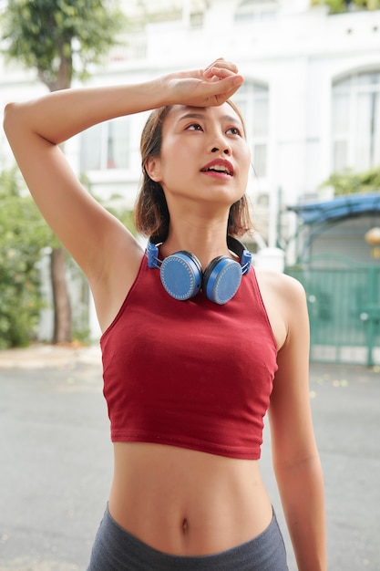 Mooie fitte jonge Aziatische sportvrouw die zweet afveegt na 's ochtends buiten te joggen