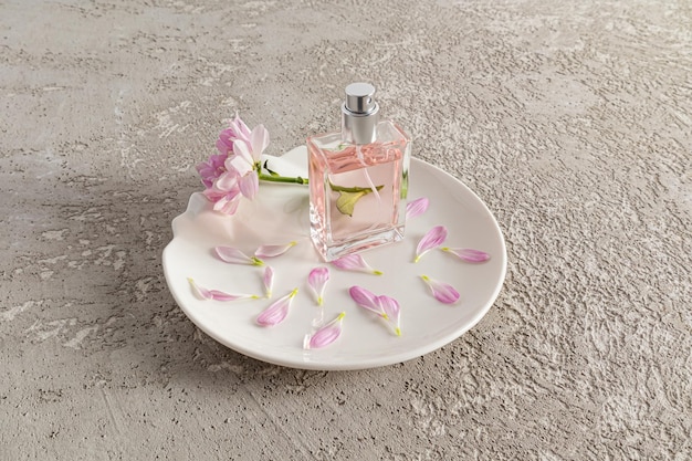 Mooie fles cosmetica of spray op een witte abstracte plaat met bloemen en chrysant bloemblaadjes grijze cement achtergrondgeurreclame