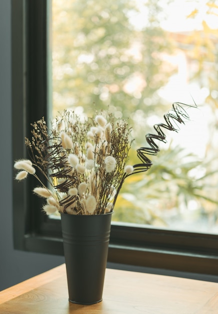 Mooie gedroogde bloemboeket in zwarte vaas met glazen venster achtergrond, slaapkamer interieur