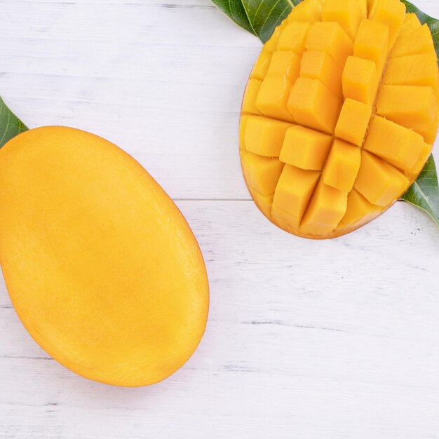 Mooie gehakte rijpe mango met groene bladeren op heldere witte kleur houten achtergrond bovenaanzicht plat lag kopieerruimte Tropisch fruit ontwerpconcept