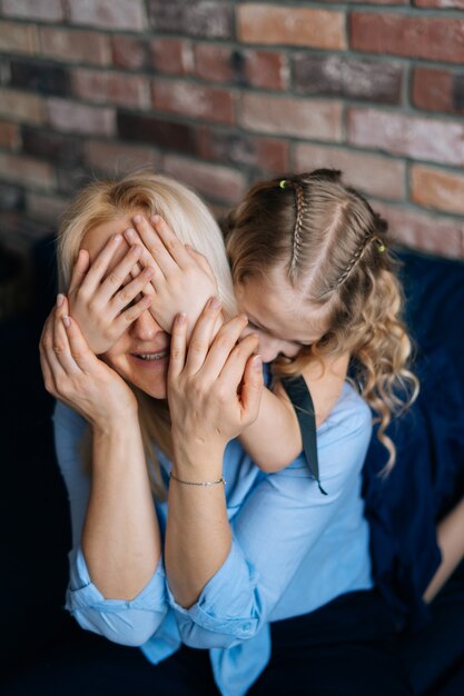 Foto mooie gekrulde dochter sluit de ogen voor haar moeder terwijl ze thuis op de bank zit in een gezellige woonkamer