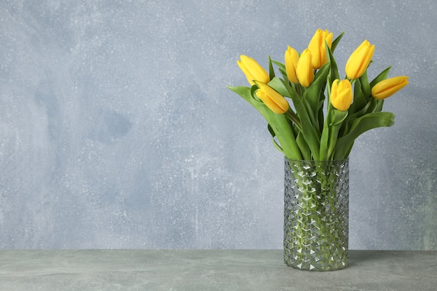 Mooie gele tulpen in een glazen vaas op grijs voor Moederdag. Ruimte voor tekst