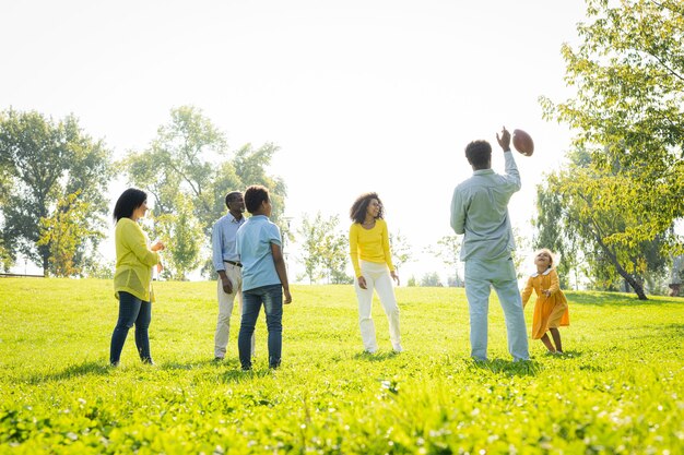 Mooie gelukkige Afro-Amerikaanse familiebinding in het park - Zwarte familie die plezier heeft in de buitenlucht, ouders en kinderen die voetbal spelen