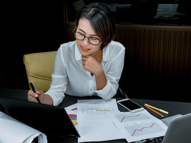 Mooie gelukkige Aziatische vrouw die overwerkt met laptopcomputer op bureau in kantoor