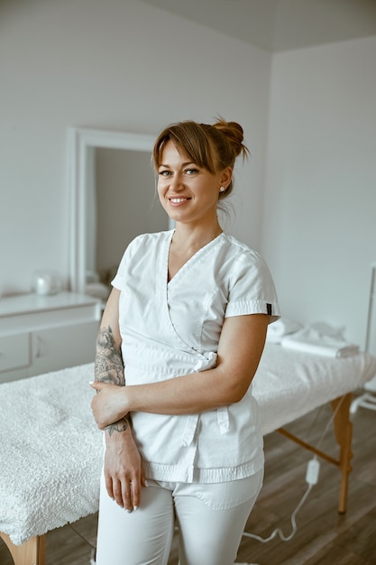 Mooie gelukkige blanke vrouwelijke masseur poseert in een witte, minimalistische, moderne behandelsalon