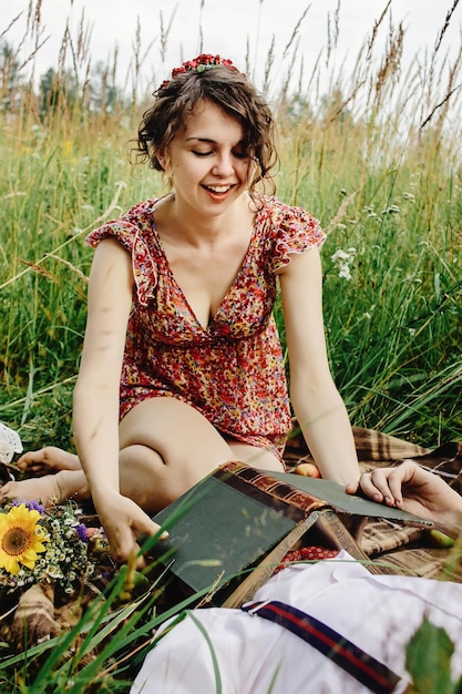 Mooie gelukkige bruid en stijlvolle retro bruidegom met plezier met boeken en ontspannende picknick in zonnige weide