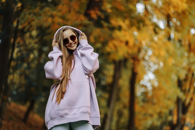 Foto mooie, gelukkige, glimlachende jonge vrouw met een roze hoodie die in het herfstseizoen in het park loopt.