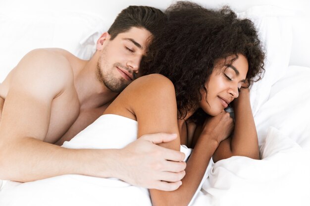 Mooie gelukkige jonge multi-etnisch paar ontspannen in bed onder deken, vrouw slapen