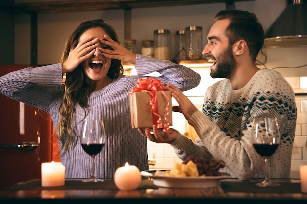 Mooie gelukkige jonge paar romantische avond samen thuis doorbrengen, drinken van rode wijn, man die een cadeau geeft