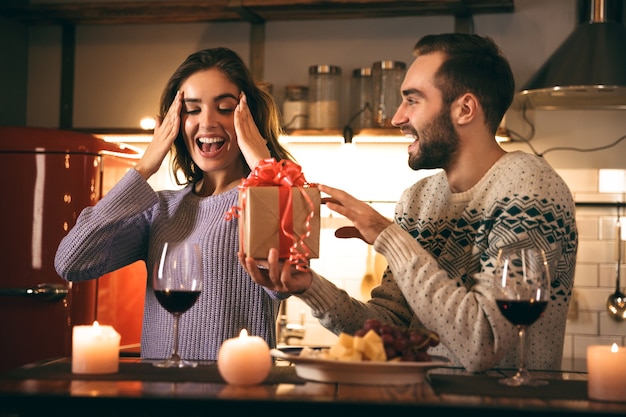 Mooie gelukkige jonge paar romantische avond samen thuis doorbrengen, drinken van rode wijn, man die een cadeau geeft