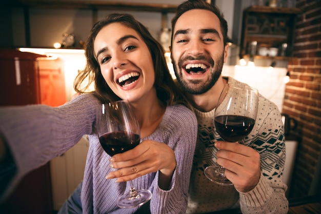 Mooie gelukkige jonge paar romantische avond samen thuis doorbrengen, rode wijn drinken, een selfie nemen