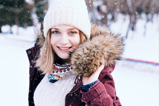 Mooie gelukkige jonge vrouw die de handschoenen van de winterhoed draagt die met sneeuwvlokken worden behandeld