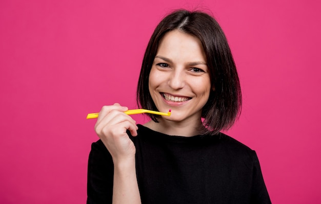 Mooie gelukkige jonge vrouw met enkele getufte tandenborstel op lege roze achtergrond