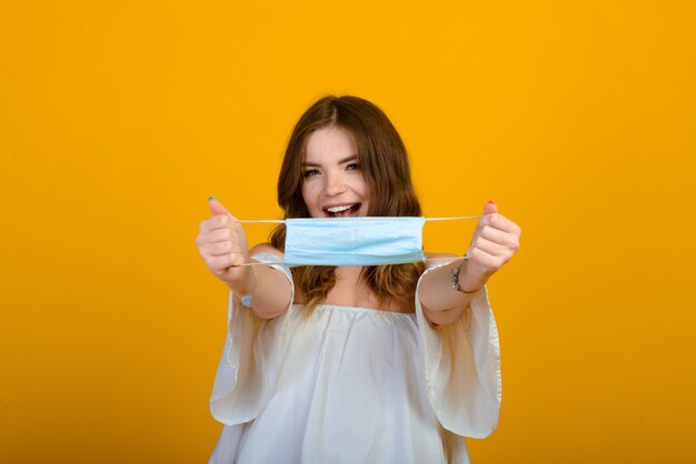 Mooie gelukkige jonge vrouw met gezichtsmasker in handen op geel