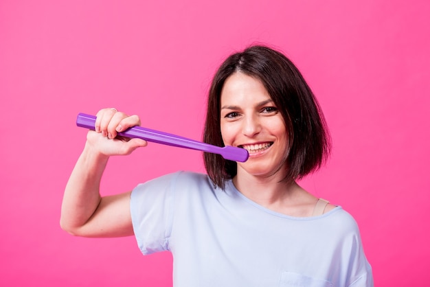 Mooie gelukkige jonge vrouw met grote tandenborstel op lege roze achtergrond