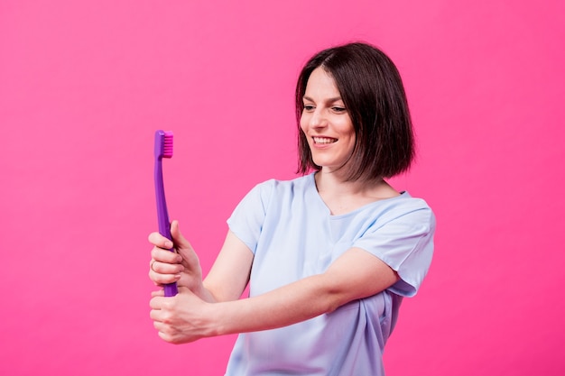 Mooie gelukkige jonge vrouw met grote tandenborstel op lege roze achtergrond
