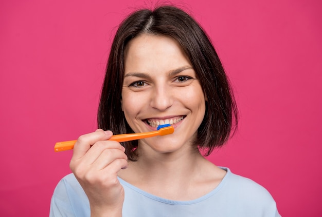 Mooie gelukkige jonge vrouw met tandenborstel op lege roze achtergrond