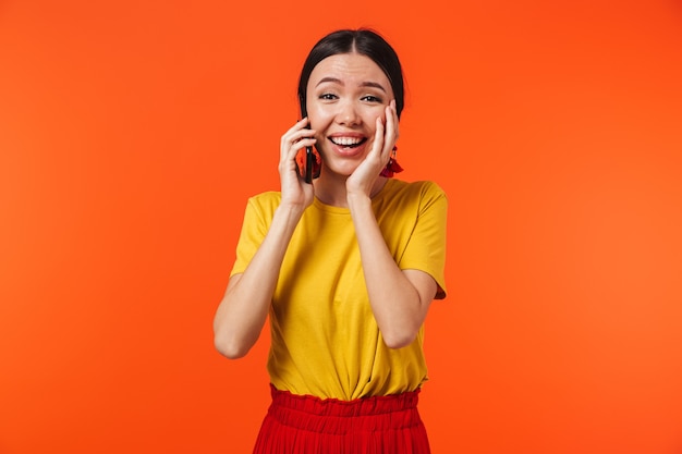 mooie gelukkige jonge vrouw poseren geïsoleerd over oranje muur praten via de mobiele telefoon.