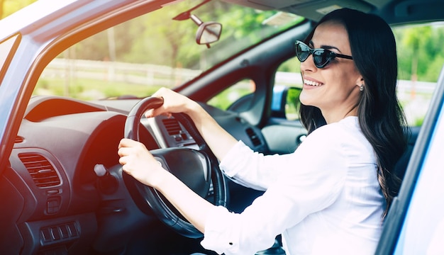 Mooie gelukkige moderne vrouwelijke bestuurder in zonnebril autorijden. Nieuw autoconcept. Bezoek bij dealer