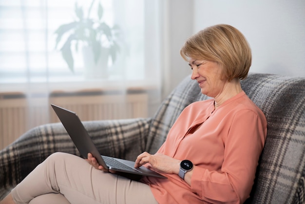 Mooie gelukkige oudere gepensioneerde senior vrouw freelancer gebruikt, werkt op laptop zittend op de bank