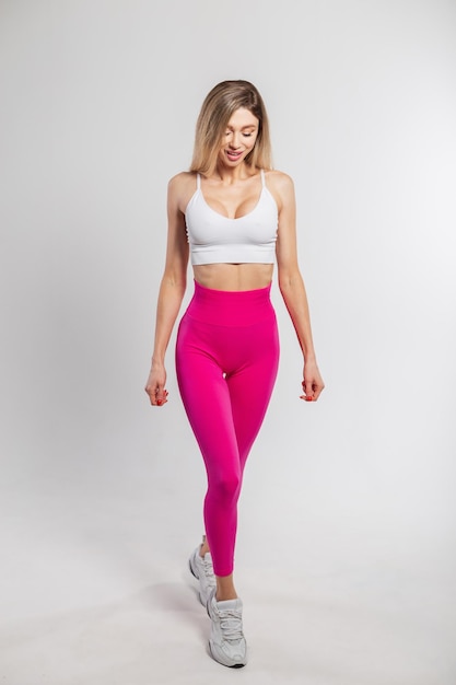 Mooie gelukkige sportieve stijlvolle fitness vrouw met slank lichaam in sportkleding met sneakers loopt op een witte achtergrond
