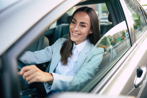 Mooie gelukkige succesvolle zakenvrouw rijdt een nieuwe moderne auto in een goed humeur. Portret schattige vrouwelijke bestuurder stuurauto met veiligheidsgordel