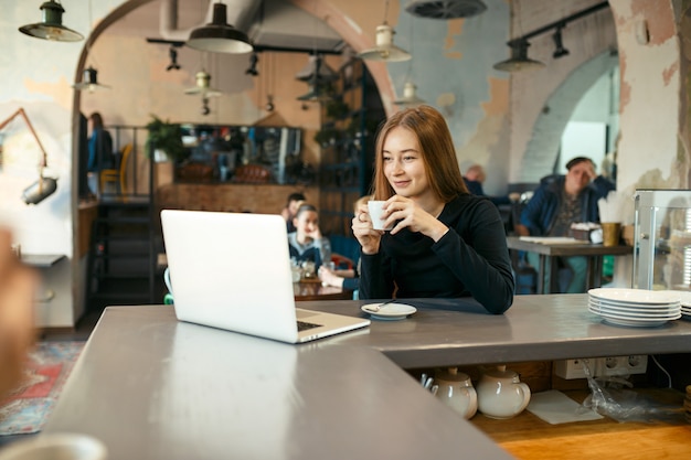 Mooie gelukkige vrouw die aan laptop computer werkt tijdens koffiepauze in koffiebar