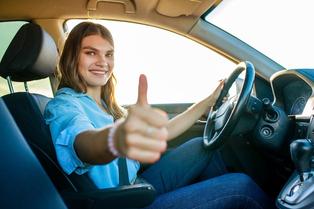 Mooie gelukkige vrouw die haar nieuwe auto bestuurt en een gebaar toont bij zonsondergang