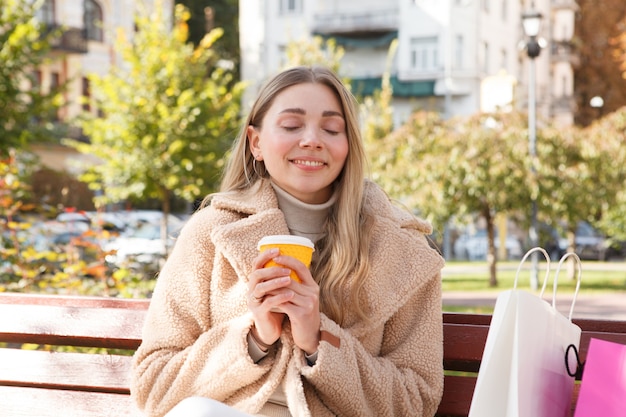 Mooie gelukkige vrouw die lacht met haar ogen dicht, genietend van koffie in het park op warme zonnige herfstdag