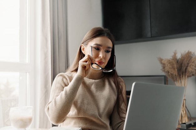 Mooie gelukkige vrouw die thuis met laptop werkt. Glimlachende zakenvrouw die een bril draagt op kantoor met behulp van computer