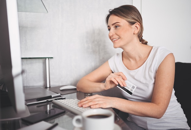 Mooie gelukkige vrouw met creditcard in de hand en met behulp van laptop computertoetsenbord. Zakenvrouw of ondernemer werken. Online winkelen, e-commerce, internetbankieren, zakgeldconcept