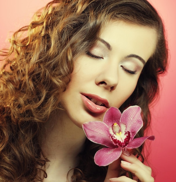 Mooie gelukkige vrouw met orchideebloem over roze achtergrond