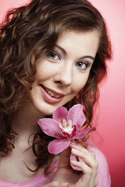 Mooie gelukkige vrouw met orchideebloem over roze achtergrond