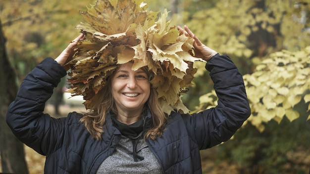 Foto mooie gelukkige vrouw van middelbare leeftijd die lacht en haar handen opsteekt. aantrekkelijke vrouw loopt in het herfstpark. selectieve focus, sfeervolle bruine tint. geweldige herfststemming