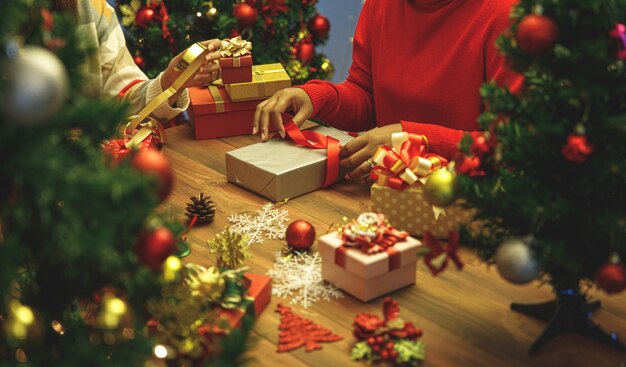 Mooie geschenkdoos verpakt en verpakt door familiegroep vrouw op trui met kleurrijk papier, lint, charmante strik om luxe kerstboom te versieren voor een gelukkige voorbereiding van het winterfeest in december