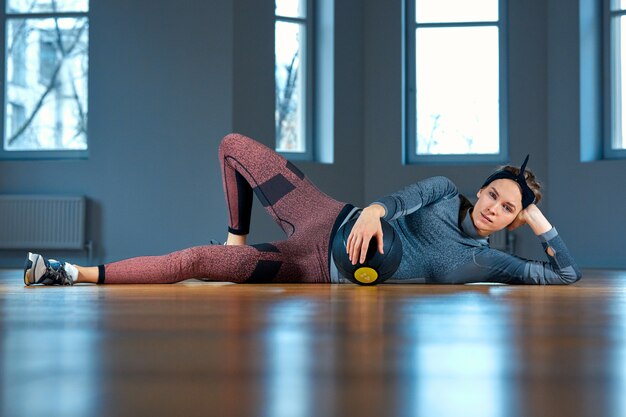 Mooie geschikte vrouw in sportkleding die terwijl het liggen op de vloer met basketbal voor venster bij levensstijl van het gymnastiek het Gezonde meisje en sportconcept stellen